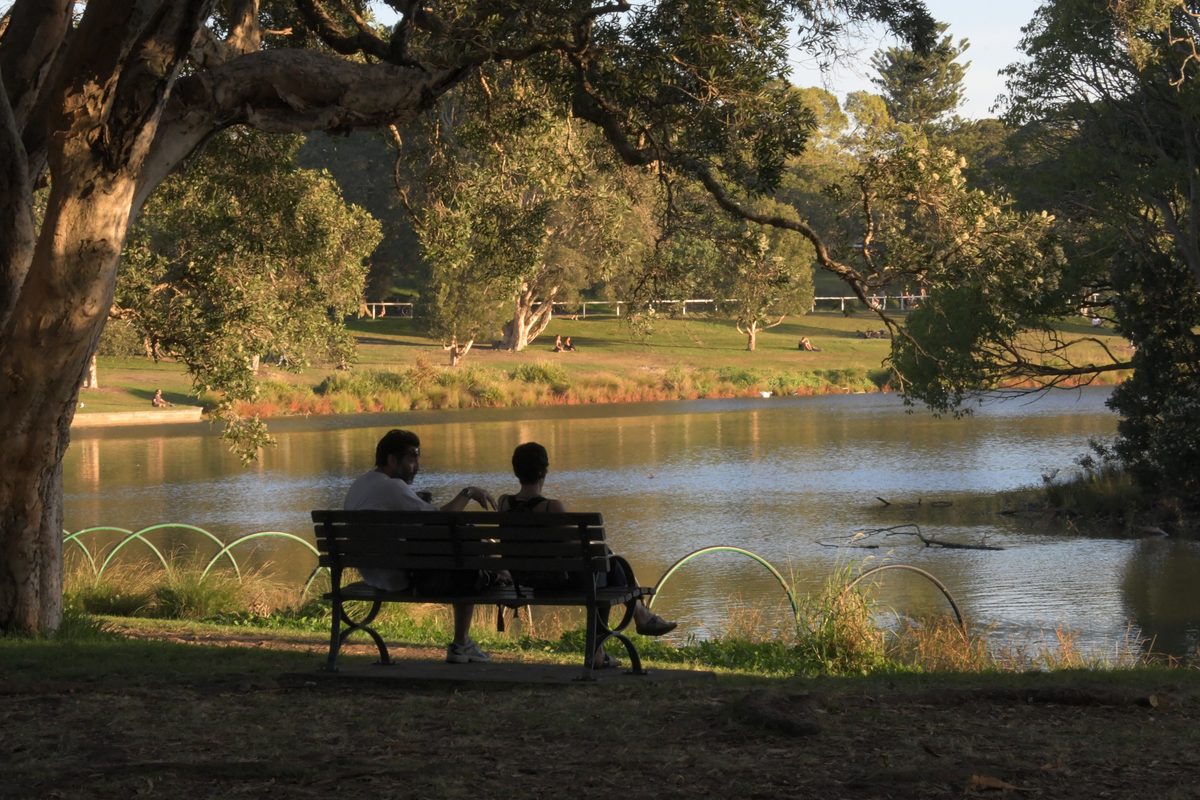 Two people on a bench by a pond in Centennial Park in the afternoon light
