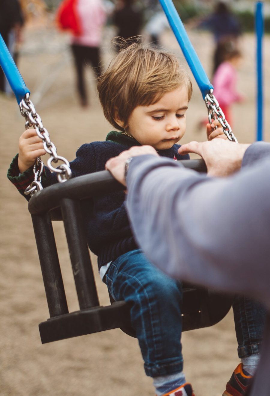 A young child on a swing, a parent's hands on the frame