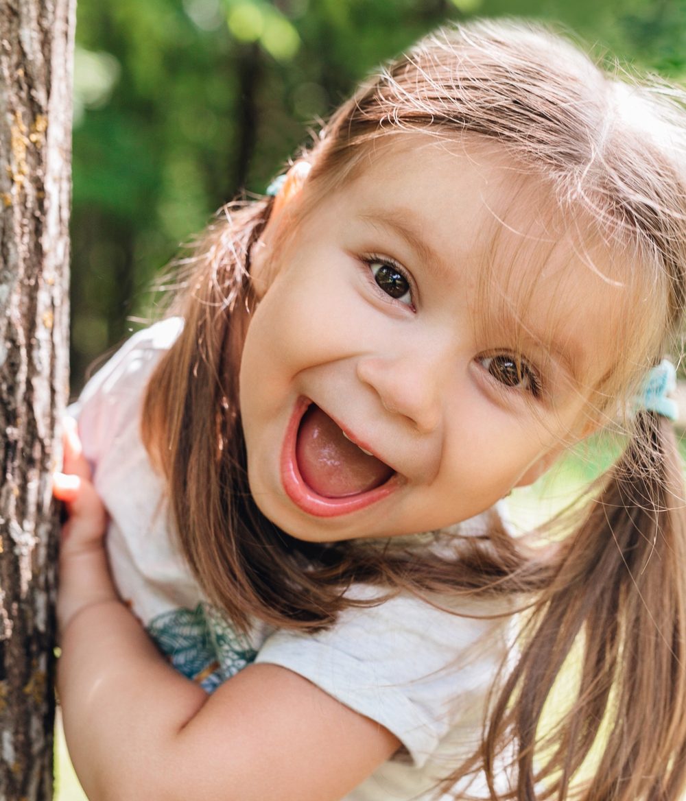 A laughing girl holding on to a tree in a park
